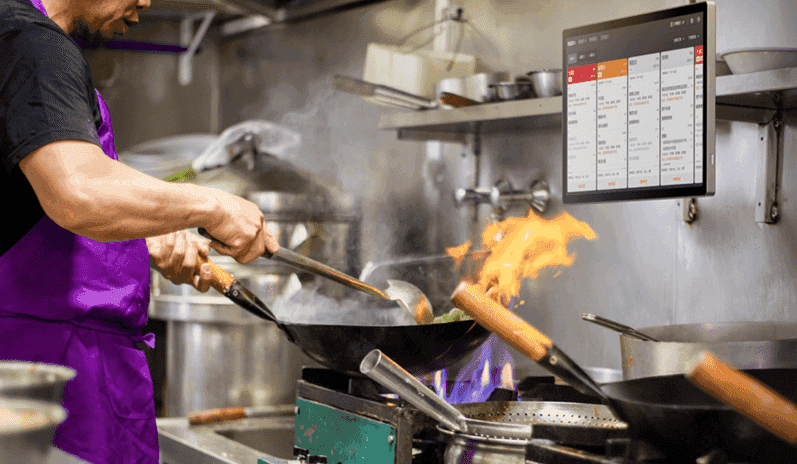 Chef using digital POS monitor in busy restaurant kitchen